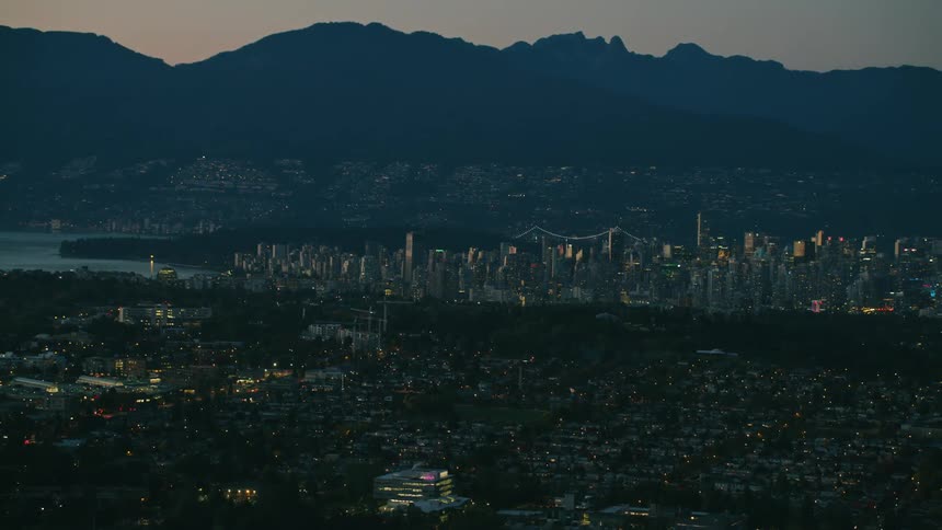 Dim city lights shine throughout city bordering water and mountains on foggy evening