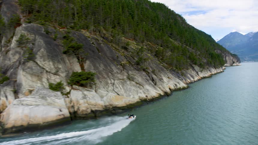 A person riding a jet ski on a turquoise blue lake surrounded by a chain of mountains