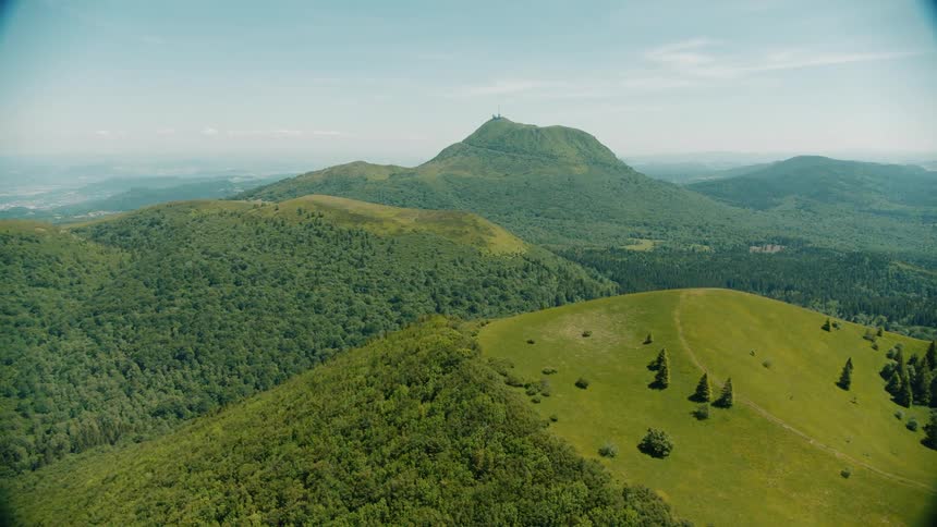 An aerial shot of mountains the closest one has a flat top with mostly grass and a few trees on it the ones further away are tree covered