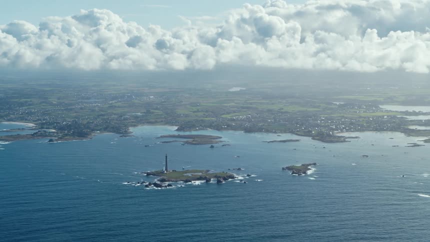 Waves roll past islands with tower and on toward shore on a cloudy day