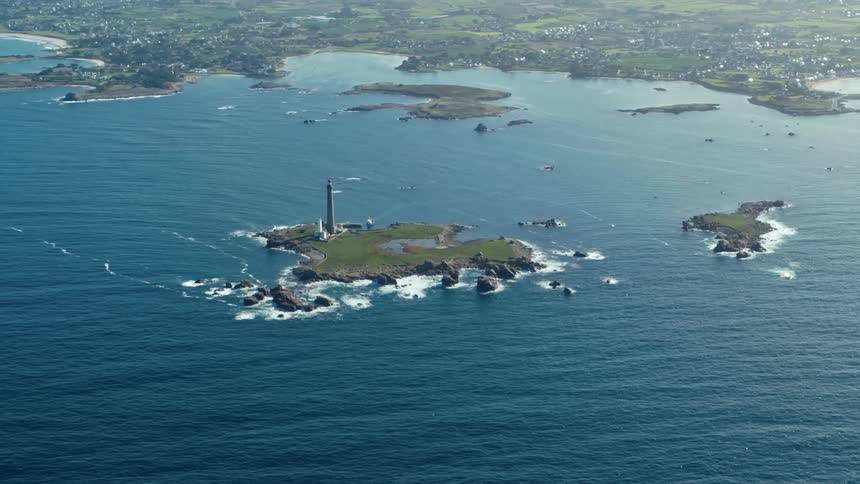 A small island with a lighthouse surrounded by water and in the background is the continent