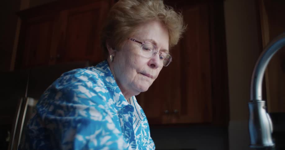 Older woman looks out window while washing dishes