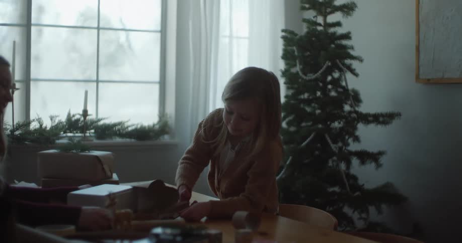 Daughter smiles while wrapping gifts with mother during christmas holiday season