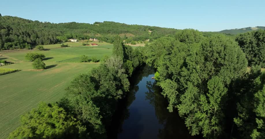 Water reflects riverbank trees as river passes by farms nestled at base of mountains