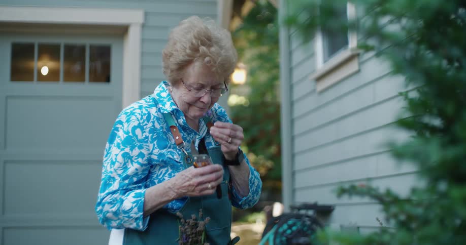 A woman is gardening and smells one of her plants