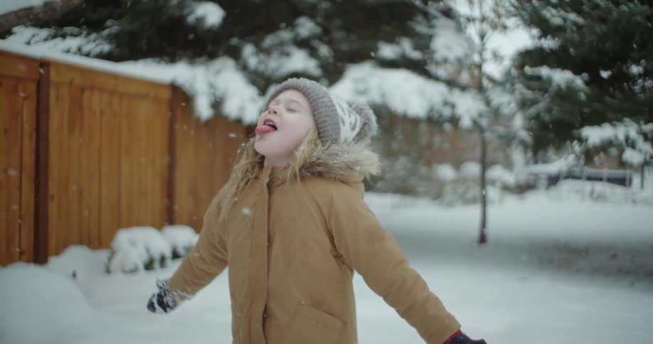 A little girl tries to catch snowflakes on tongue as it snows