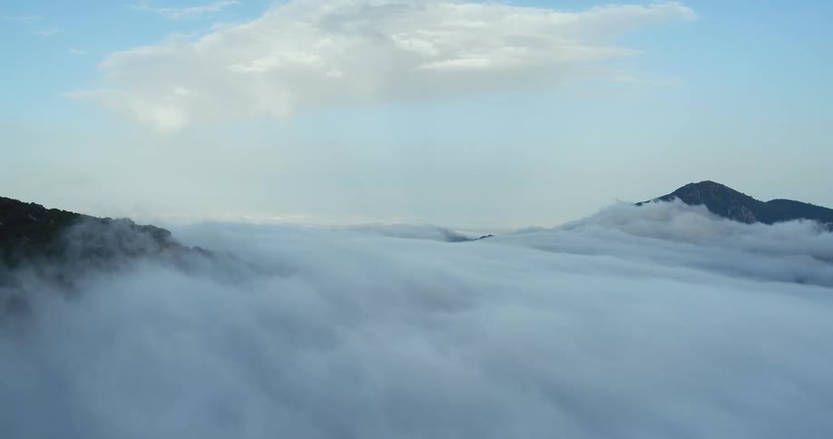 Stony mountain peaks are barely showing above a shroud of thick cloud below a blue sky with more clouds in it