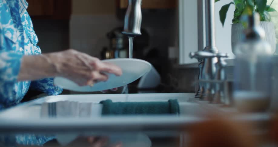 The hands of an elderly person washing a dish in the sink