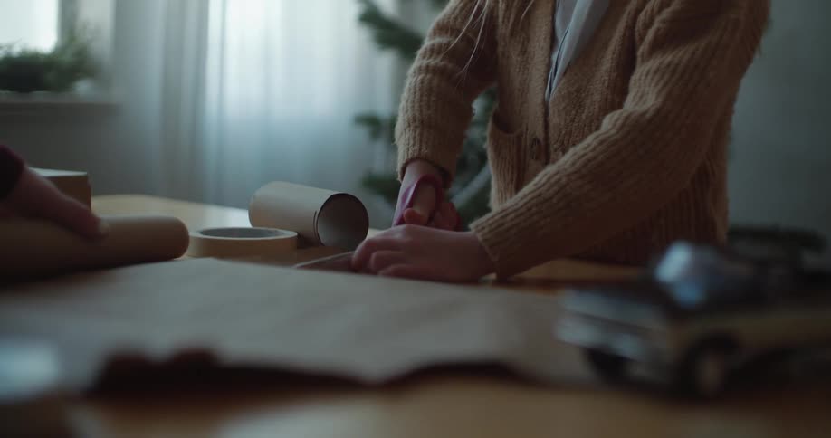 Daughter cuts paper standing at table near christmas tree