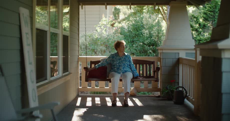 Woman in a blue shirt and white pants sits on porch swing