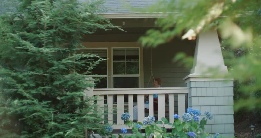Elderly woman sits on a hanging chair on the porch