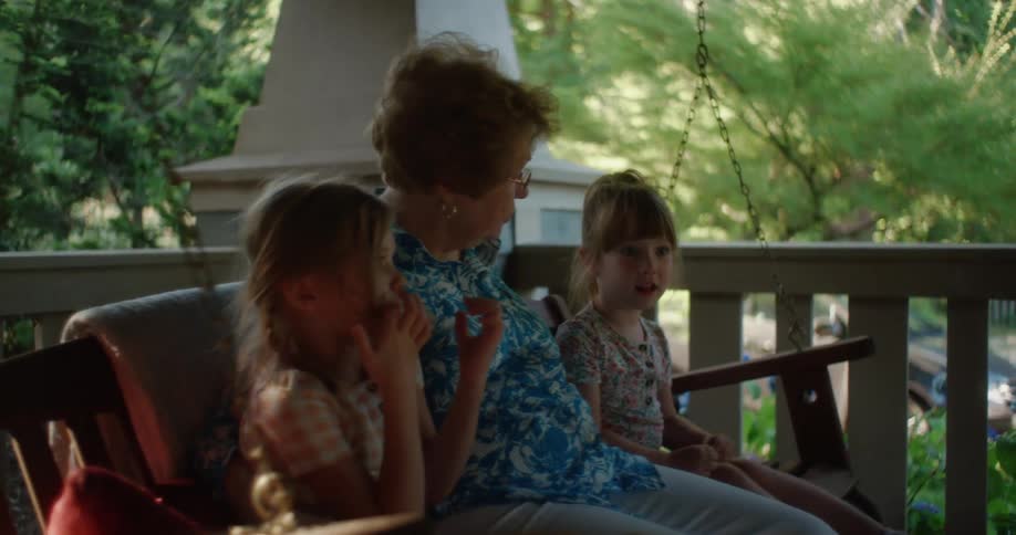 Grandmother and granddaughters sit on porch swing