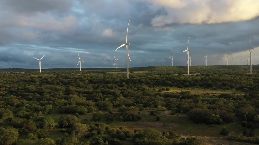 Wind turbines tower over wooded area under darkening dense clouds