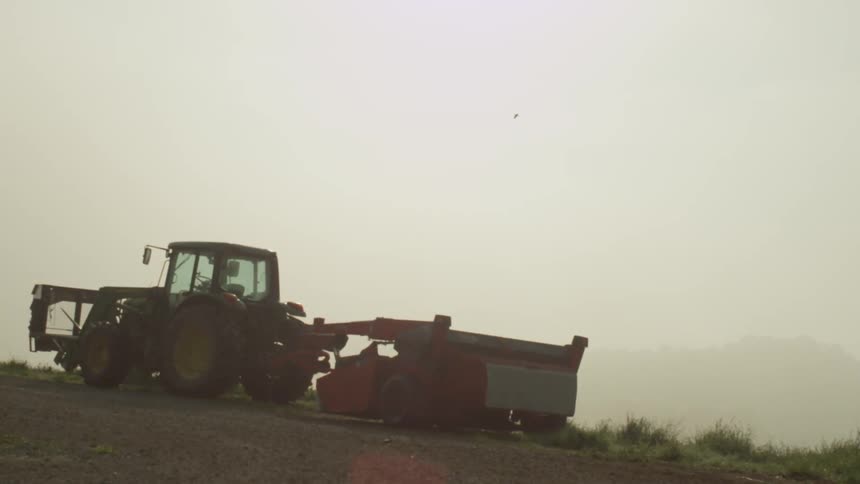 A farm vehicle is on a hill on a cloudy day