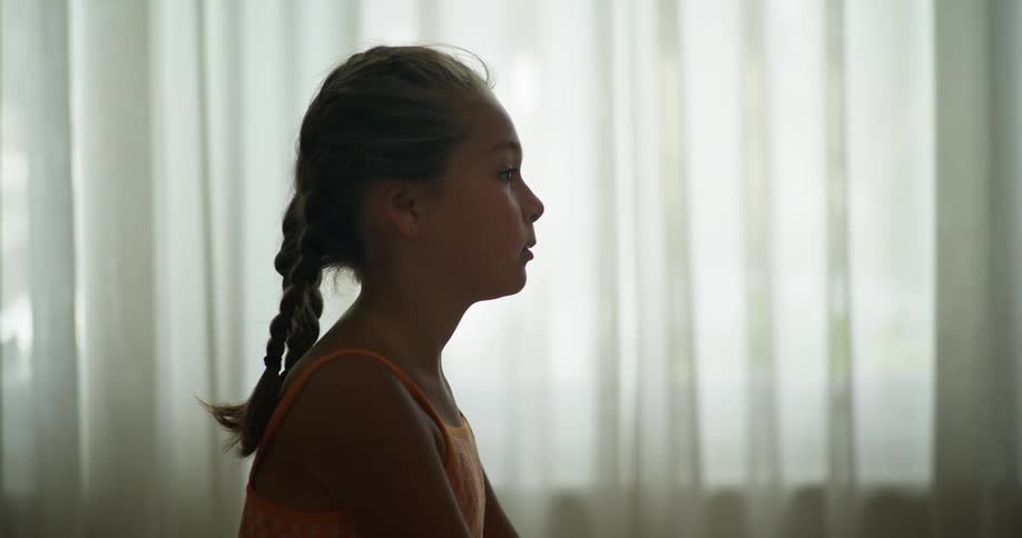 A child sits by a window watching TV