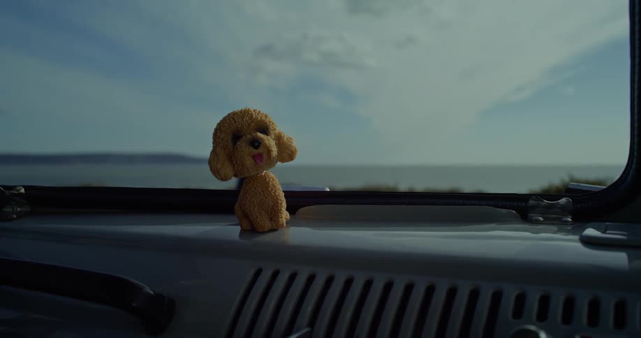 Toy dog sits on the dashboard of a car parked next to the ocean