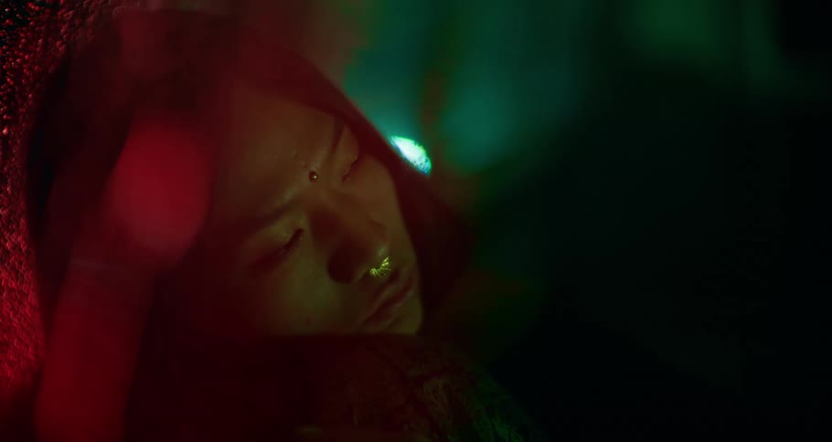 A woman rests in her car, in the dark as rain runs down the windshield