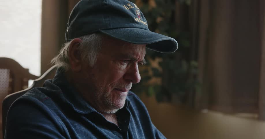 An elderly man indoor thinking while sitting on a chair at midday