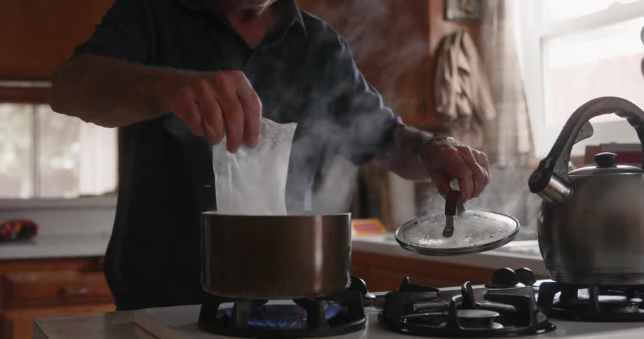 An elderly person putting rice in a saucepan to cook with hot water