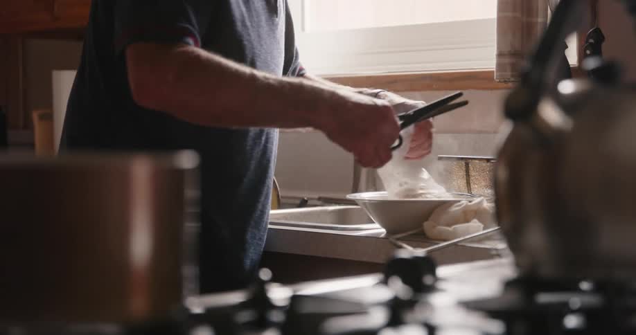 A man holding a pair of scissors and placing food into a bowl for cooking