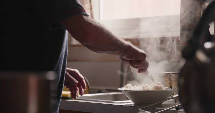 A man wearing a dark tshirt mixes rice in a bowl in the kitchen