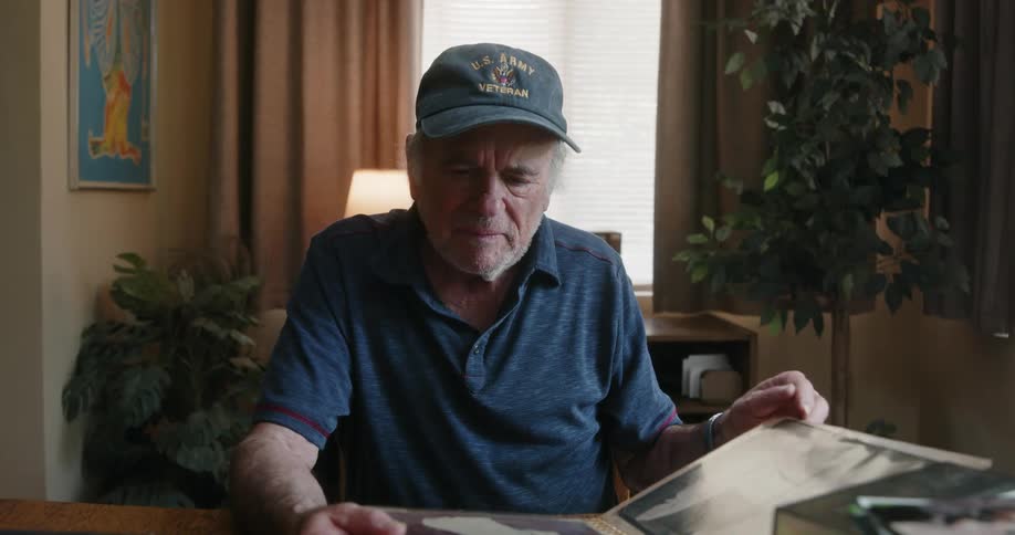 A mans old bone is turning the pages of a book of portraits as he sits down