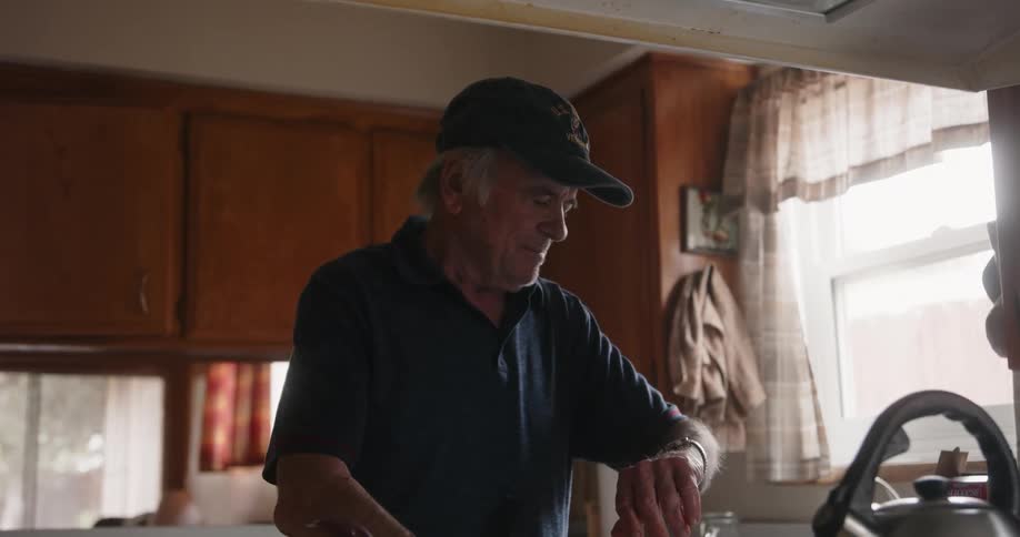 Elderly man with a cap and t shirt cooks in the kitchen
