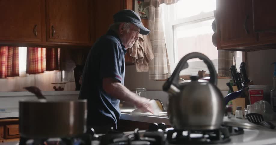 Man wearing a baseball cap cleans the kitchen sink