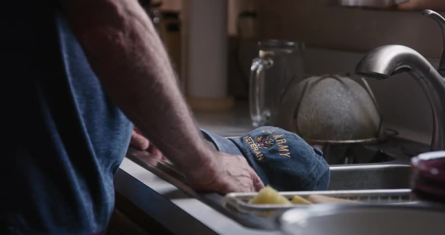 A man lifts his hat up by the sink