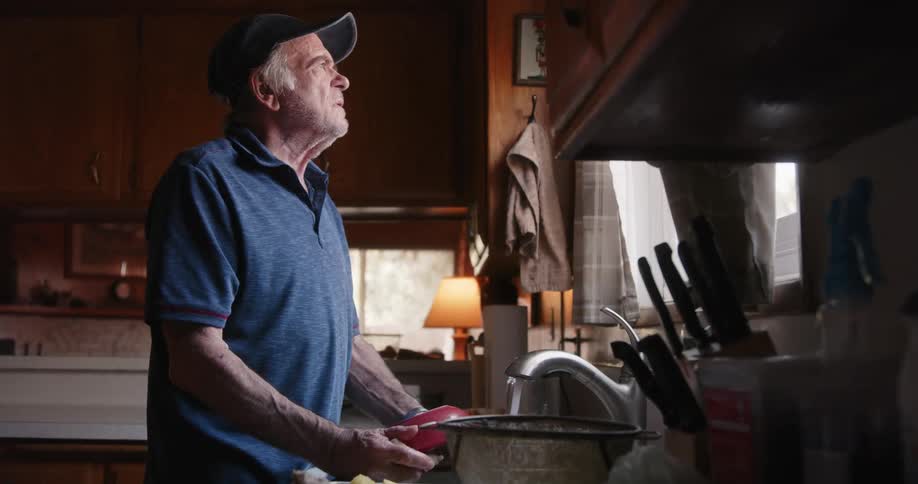 Man wearing a baseball cap cleans the dishes in the kitchen sink