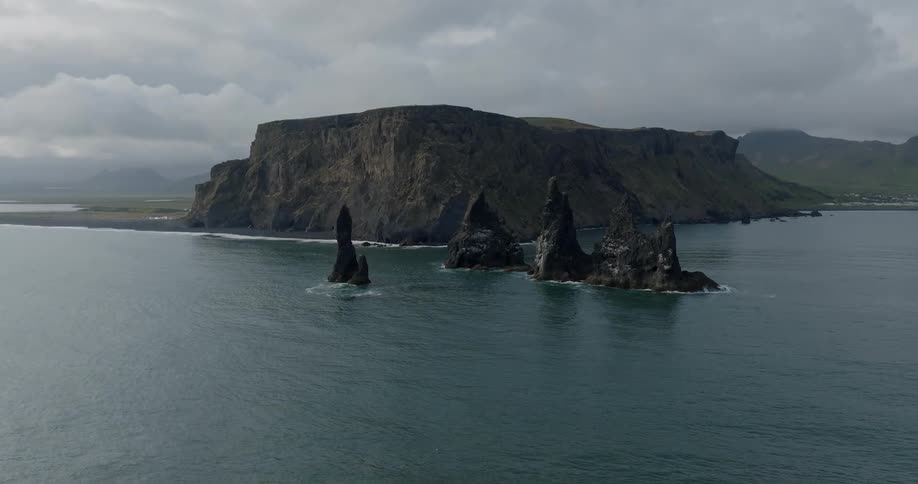 Small rocky structures jut out of the water in front of a larger rocky structure
