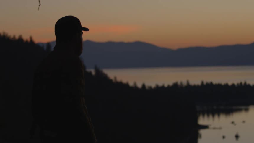 A man i standing by a lake at dawn