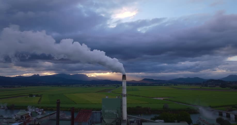 A factory with a white tower emitting smoke in a rural area