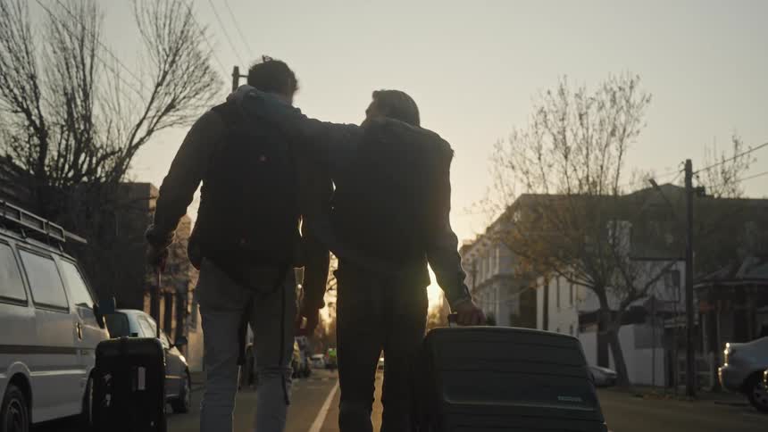 Two men drag their luggage through the street