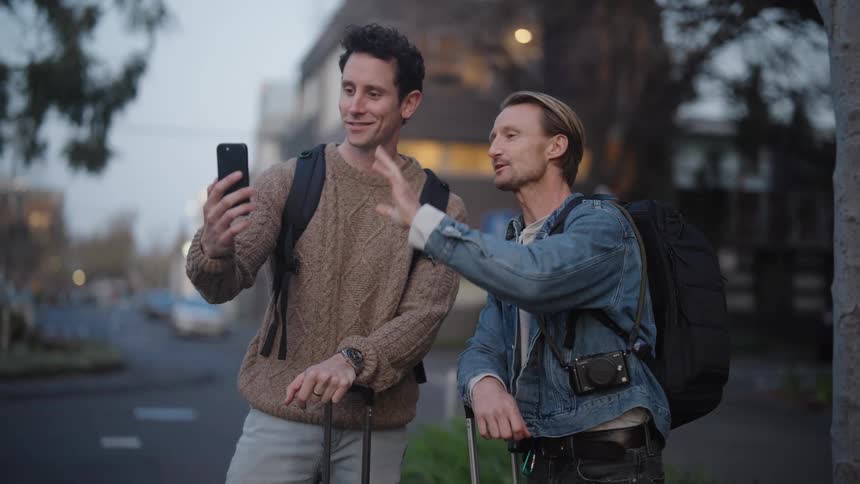 Two men side by side talking on their cell phones and one of them blowing a smiling kiss