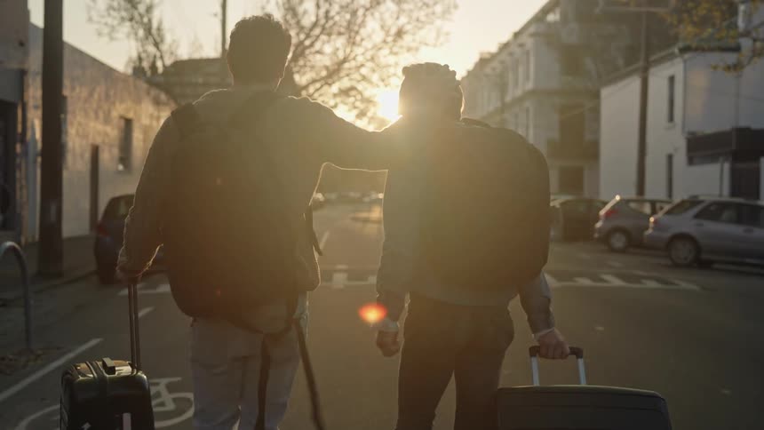 Two happy tourists carry their luggage on the streets of a town at sunset