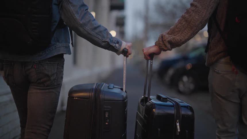 Two people walking on the sidewalk with their travel bags