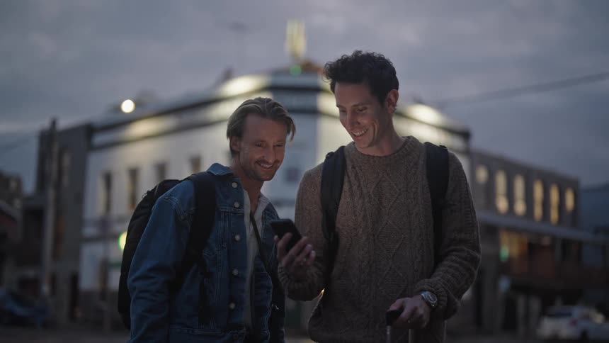 Portrait of two people conversing and looking at something on a cellphone in an outdoor city environment