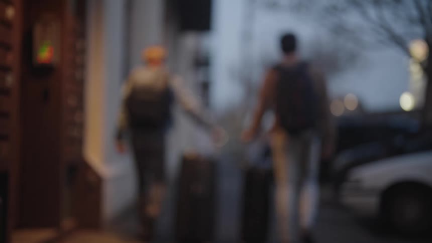 People walking with two large suitcases on the sidewalk