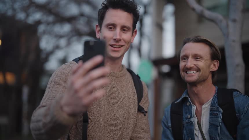 Friends on street with camera and backpacks share smartphone during video call