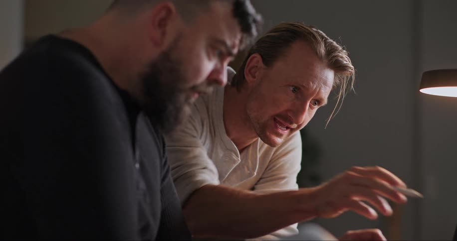 Two men sitting and working on a laptop while conversing and smiling