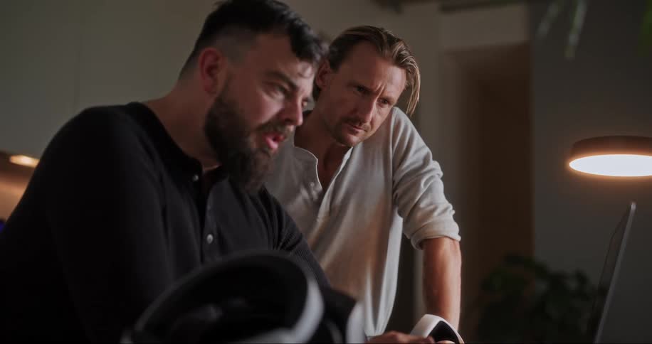 Two men working at home talk in front of a laptop