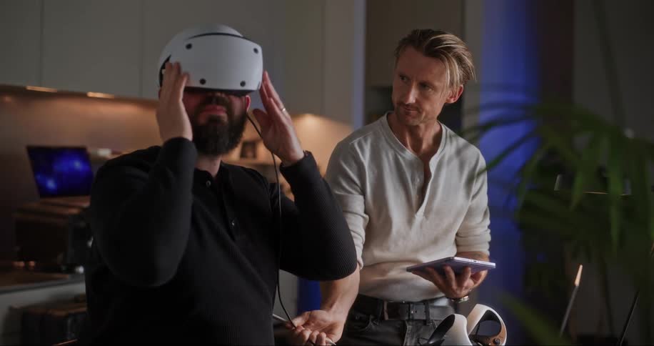 A man puts on a virtual reality headset while another man uses a tablet
