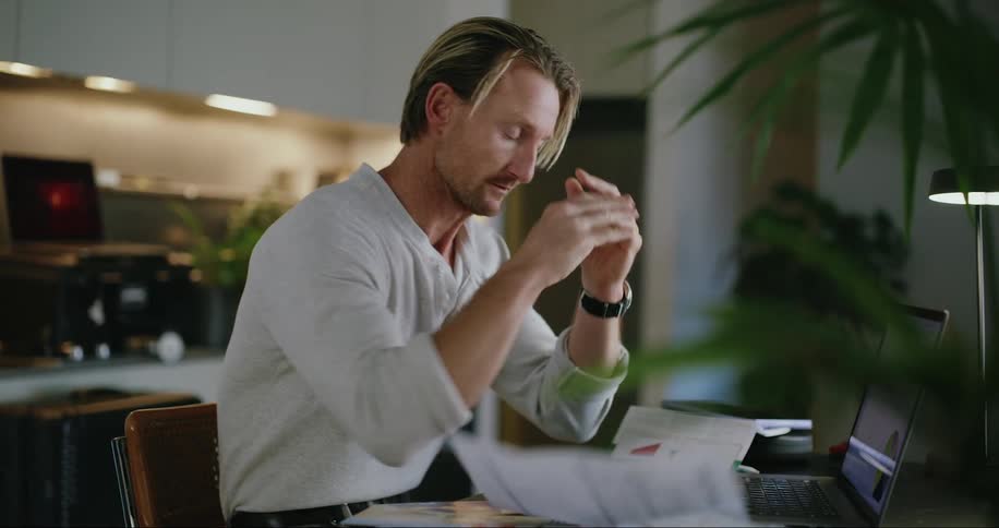 A seated man picks up a paper and when he reads it he gets nervous and throws it on the floor