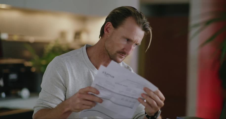 A man sitting and reading a document with a somewhat disheartened expression