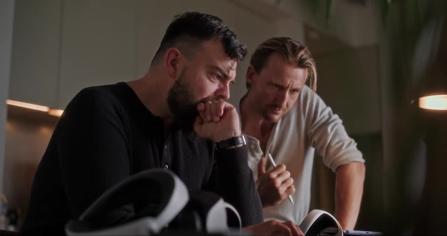 Two men talk and look at a laptop together