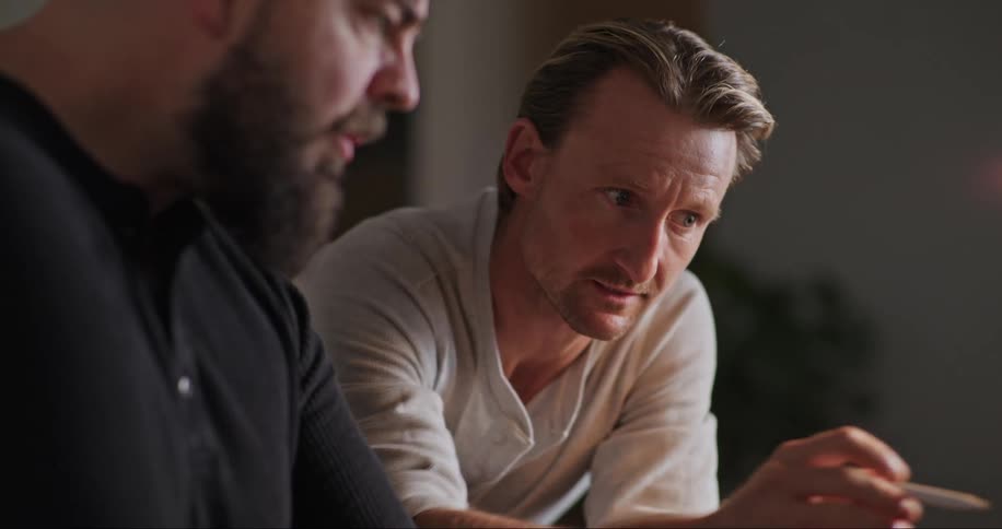 Two men talk while looking at a laptop