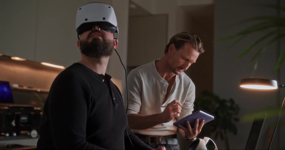A man is testing a virtual reality headset while another man takes notes