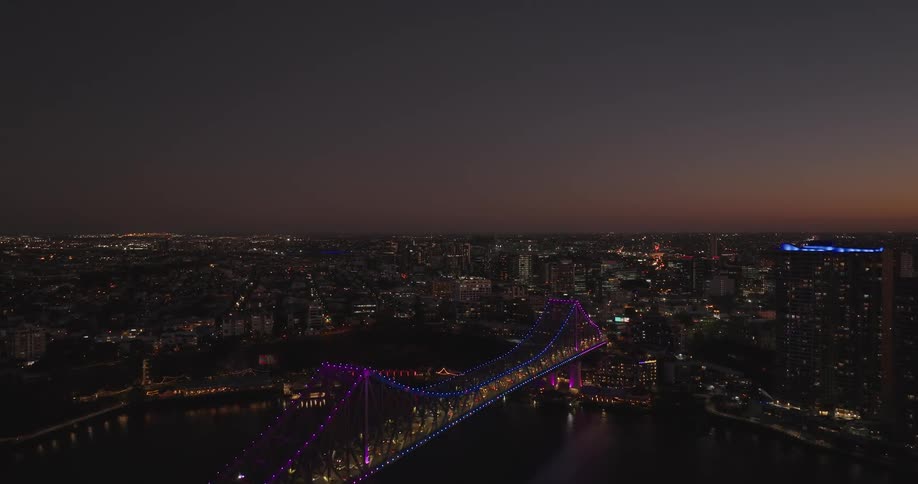 Aerial view of a metropolis by the seaside at night with bridges and vehicles passing through