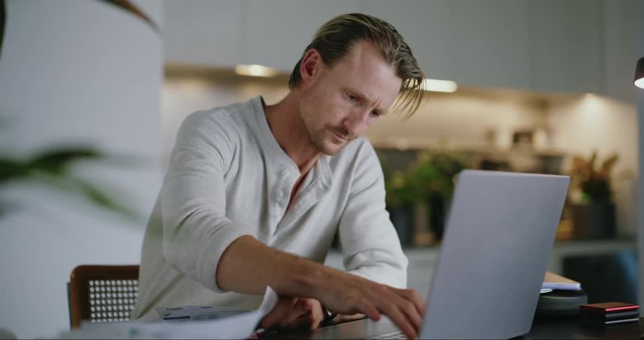A man reads a paper and types on his laptop